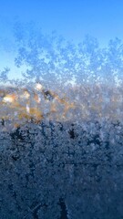 Frost crystals on glass with soft blue sky and warm sunlight, macro winter pattern