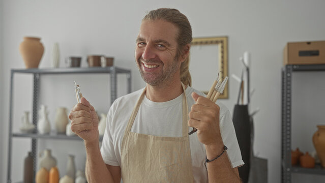 Man with apron holds pottery tool and gives thumbs up gesture in a studio pottery class filled with clay vases; confidence.
