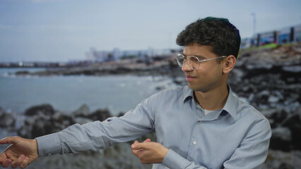 Fototapeta premium Man pointing finger at seaside shoreline while looking toward the horizon wearing a blue shirt; serenity reflection calm tranquility.