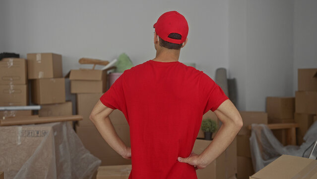 Young hispanic delivery man holds lower back for backache in new home with moving boxes; exhaustion.