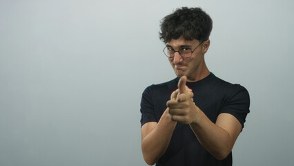 Man pointing finger at camera with visible hands and round glasses in pale gray studio, young wearing black t shirt; playful invitation.