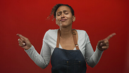 Woman dancing with fingers pointing and eyes closed in studio against a red backdrop; joy celebration.