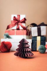 A small folded paper tree placed in front of wrapped gifts and ribbons creating a soft festive holiday Christmas scene with warm tones. Closeup