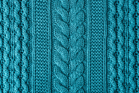 A closeup view of a teal knitted fabric showing thick braided cables and soft textured wool fibers. Christmas sweater background, top view