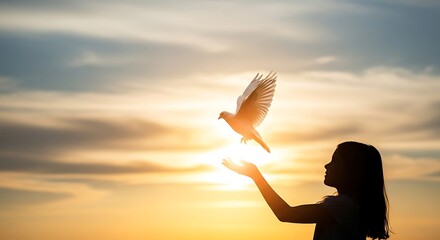 Silhouette of girl releasing white dove at sunset with glowing light bird flying