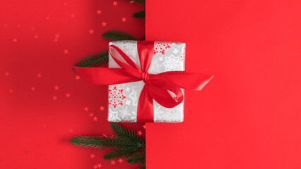 Red Christmas background. A gift box with a red snowflake pattern and a bright red ribbon framed by fir branches on a red background. Perfect for holiday promotions or Christmas cards.
