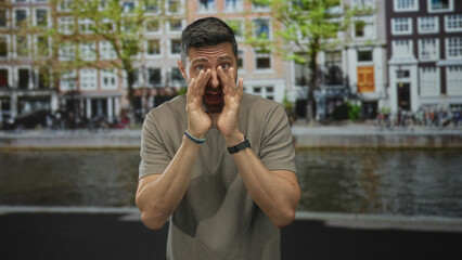Man cupping hands to mouth shouting across canal on amsterdam street with water and riverside buildings visible; urgency warning.