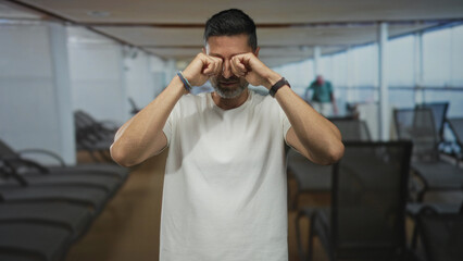 Man rubbing eyes with fists on a cruise ship deck with lounge chairs and panoramic windows; fatigue...
