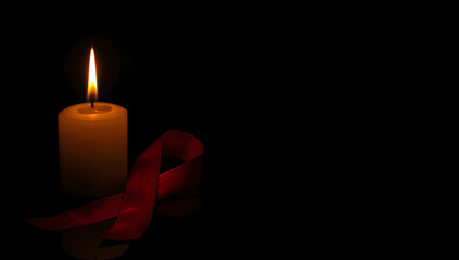 A single burning candle flame and a red ribbon, a solemn symbol of solidarity and remembrance for World AIDS Day on a dark background