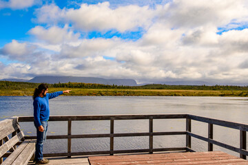 Young man on viewing platform along a forest trail  in Gros Morne National Park Newfoundland points toward Western Brook Pond on a bright fall day room for text