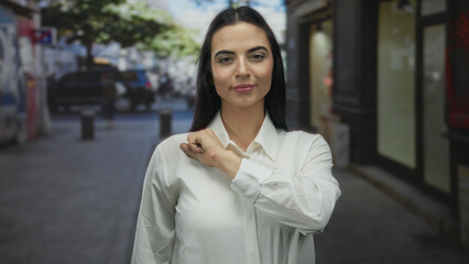 Young hispanic woman extends fist towards camera on urban street with blurred background, exuding...