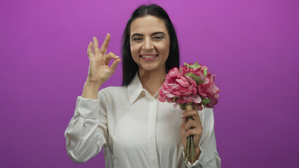 Woman holding a pink bouquet making an ok gesture against a vibrant pink background radiating positivity and elegance.