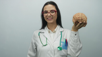 Hispanic female doctor with a stethoscope holds a brain model against a plain white wall background.