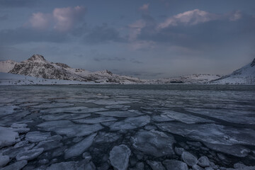 Frozen Arctic Lake with Layered Sea Ice and Snow-Covered Mountains under a Soft Winter Sky in Northern Norway