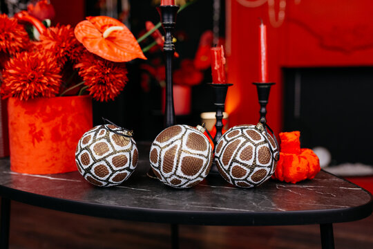 Christmas balls decorated with snake skin lie on a dark table surrounded by red interior items: candles, vases, and a fireplace. A festive setting for a living room or the office of a creative agency