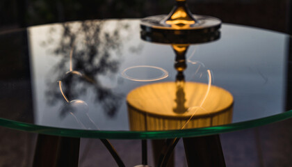 Glass table reflects tree branches and golden object at dusk.