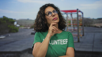 Woman volunteer in green shirt thinking outdoors with gym equipment in background.