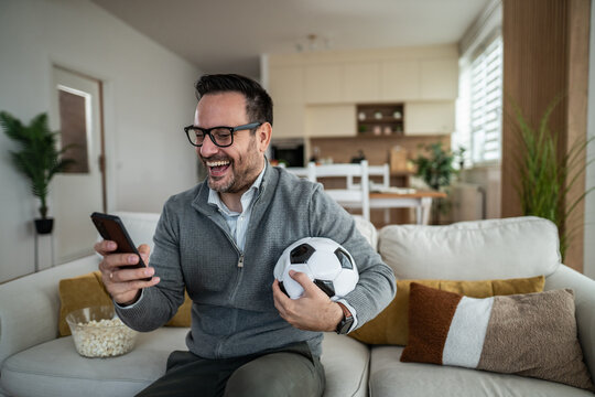 Man laughing at home watching soccer on phone