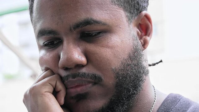 Young Black Man With Braided Hair And Beard Looking Down With Thoughtful Expression And Hand Resting On Face In Quiet Moment Of Reflection