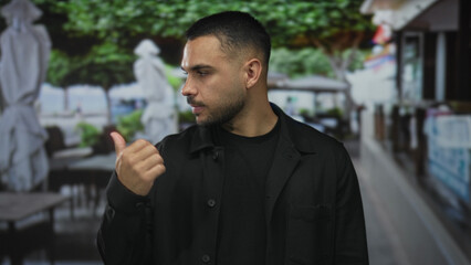 Man shows bare thumb up gesture on building terrace overlooking blurred tables and umbrellas; optimism.