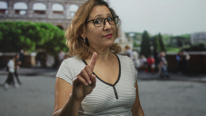 Woman points finger at camera in coliseum building outdoors tourist site near roman ruins; warning authority.