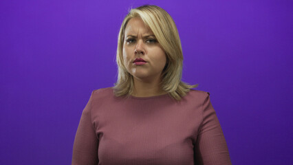 Blonde woman cups ear with hand in purple studio setting while leaning forward in attentive pose; curiosity.