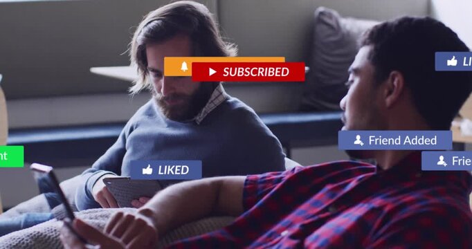 Two men tapping phone and tablet on couch, causing animated social UI badges and discussing content