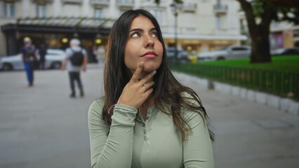 Hispanic woman contemplating outdoors on a bustling city street with blurred pedestrians in the...