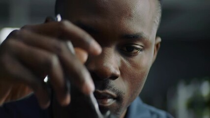 Close-up of a focused African man holding pen, concentrated on technology repair, device, hardware, engineering, electronics, and precision.