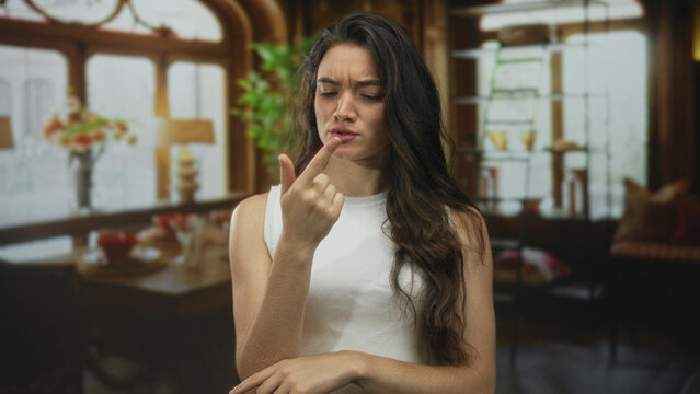 Young hispanic woman wearing white tank top counts fingers in a renovated building; learning focus concentration.