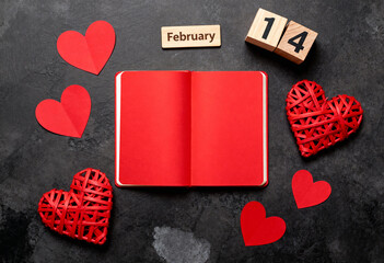 Red open notebook with blank pages on a dark background, surrounded by red paper hearts and rattan hearts, accompanied by a wooden calendar showing February 14