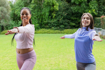Diverse female friends practicing standing balance yoga pose on backyard lawn wearing athletic wear