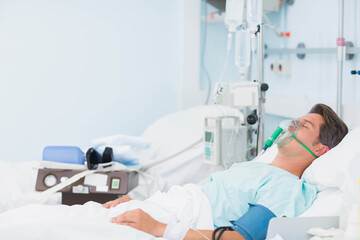 Male patient lying supine on hospital bed receiving oxygen mask and IV pump, copy space