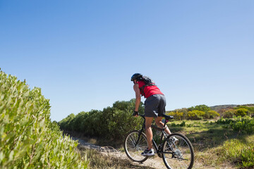 Obraz premium Mature adult man riding mountain bike on sandy trail wearing red top, helmet, pack, copy space