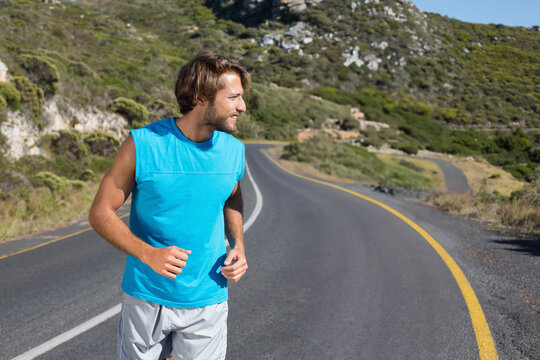 Male runner jogging left on winding two-lane road, wearing teal top, passing yellow and white lines - Powered by Adobe