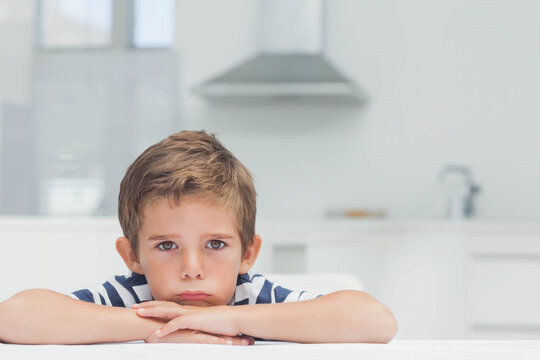 Child boy resting chin on folded arms, looking forward at white countertop wearing striped shirt