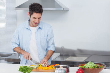 Man chopping vegetables on cutting board in kitchen, wearing light blue shirt, using chef's knife