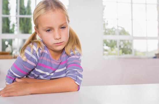 Female child sitting at white desk leaning in striped top gazing out windows at windowsill plant