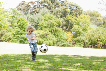 Obraz premium Boy child kicking black-white soccer ball on grassy park lawn wearing white T-shirt jeans and shoes