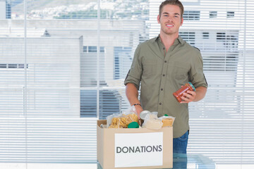 Male standing in green shirt holding jar over DONATIONS box at office, copy space