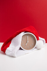 Alarm clock covered with santa hat on red and white background. Holiday Countdown.