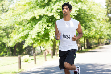 Asian man running along paved park path wearing sleeveless shirt with bib 1634 and shorts