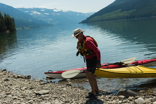 Senior man in life jacket pulling yellow kayak with white paddle, red kayak nearby, copy space