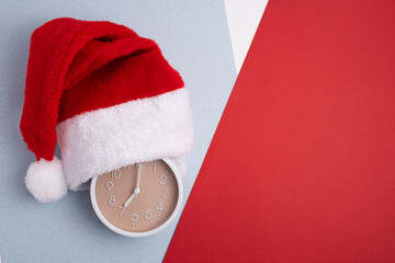  Alarm clock covered with santa hat on red and white background. Holiday Countdown.