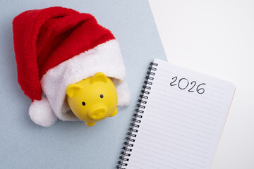 New Year 2026 financial plan. Piggy bank in santa hat next to notebook for budgeting