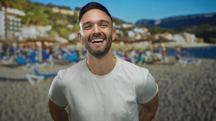 Fototapeta premium Young hispanic man smiling at the beach with sun umbrellas and scenic coastline backdrop, capturing the essence of a relaxed seaside vacation day.