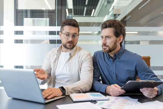 Two male business partners discussing work and reviewing data on a laptop, actively brainstorming ideas and planning a new project during an office meeting