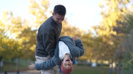 Happy father playing with his smiling son, holding him upside down while enjoying a sunny autumn day