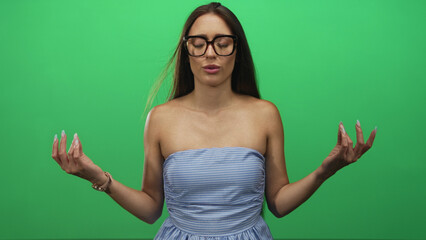 Woman wearing glasses and a blue striped strapless dress meditating with raised hands and closed...