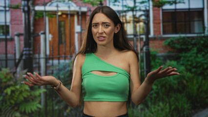 Woman in green crop top with exposed midriff touches hair while frowning at building entrance;...
